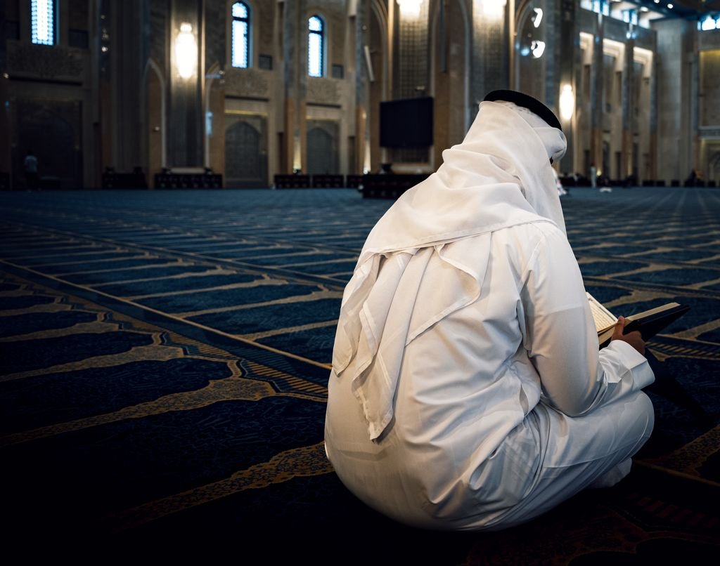A man dressed in traditional clothing praying inside a grand mosque in Al Ain City, offering a serene atmosphere.