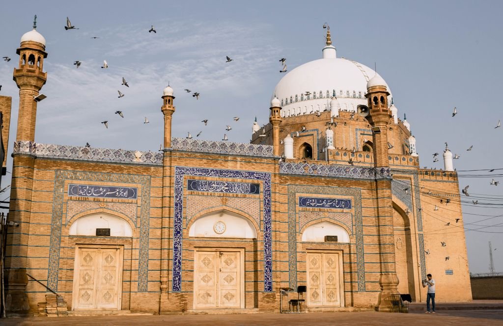A stunning view of the Bahauddin Zakariya Shrine in Multan with flying pigeons against a clear sky.