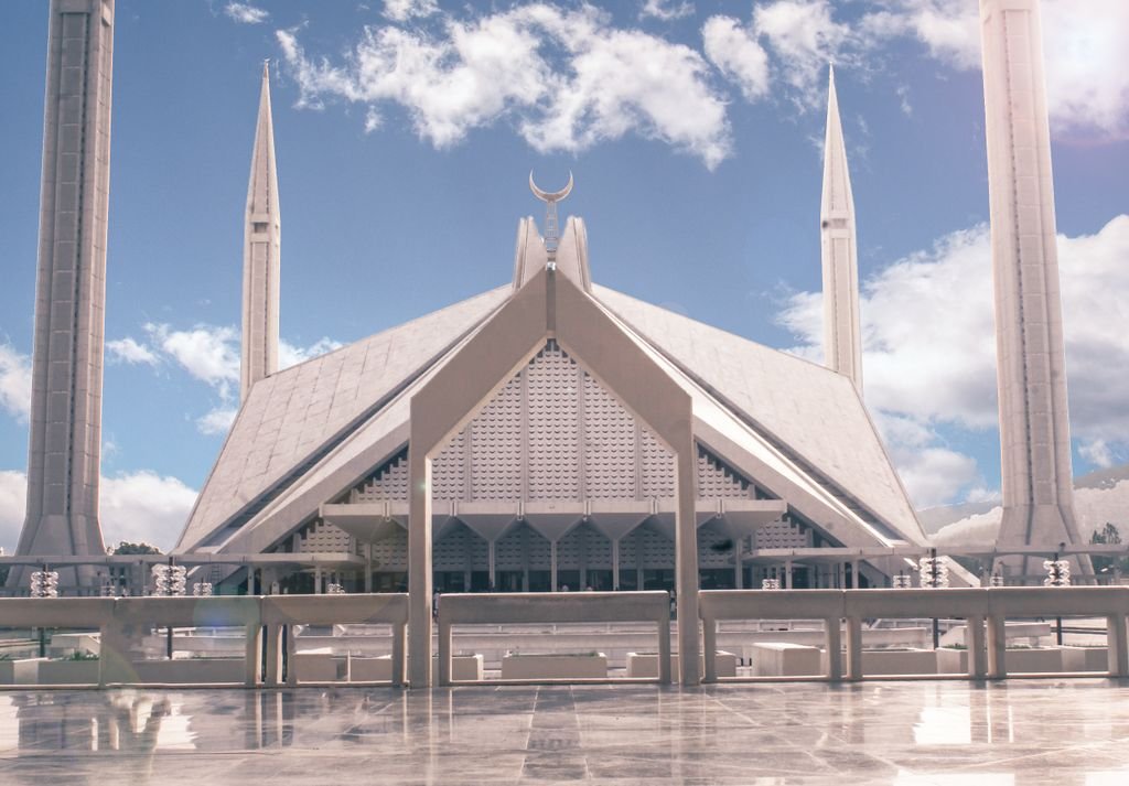 Iconic view of Faisal Mosque in Islamabad, Pakistan, under a bright blue sky with clouds.