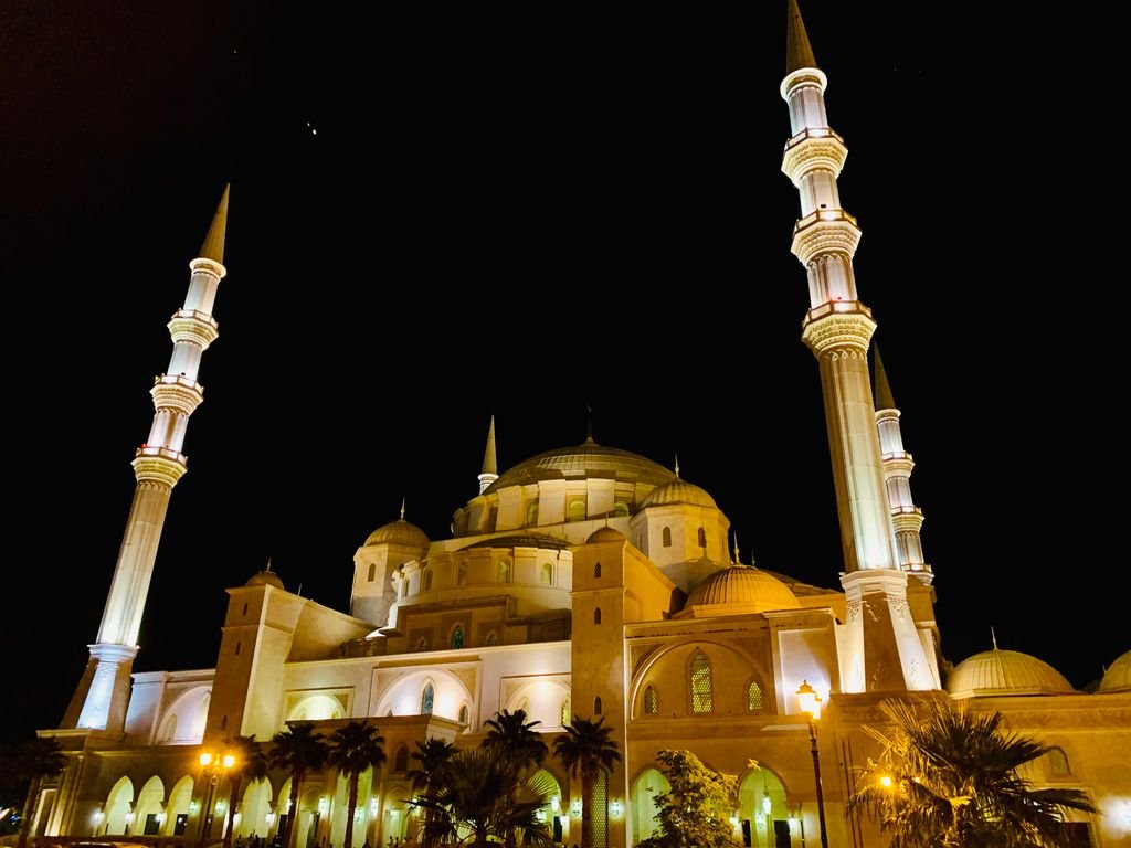 Stunning night view of an illuminated mosque of sharjah with towering minarets against a clear night sky.