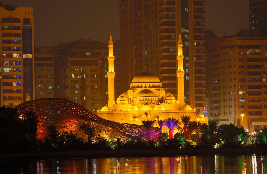 Stunning night view of the Al Noor Mosque with vibrant city backdrop in Sharjah, UAE.